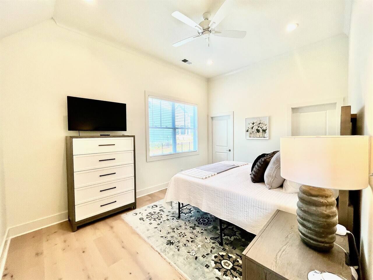 A bedroom with a bed, a dresser, a TV, a lamp, and a window.