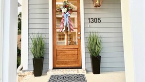 Puerta principal con el número 1305, un felpudo y dos macetas con plantas.