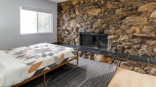 Ein Schlafzimmer mit Steingemäuer, Kamin, Bett mit gemustertem Überwurf und Fenster.