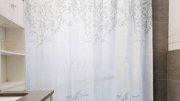 A bathroom with a toilet, a green rug, a shower curtain with a leaf pattern, and a towel rack.