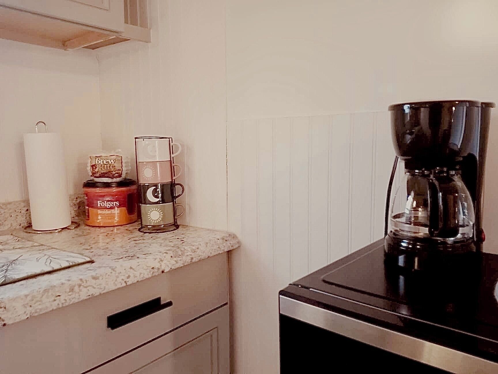 Una cucina con una macchina per il caffè, una tazza di vetro e un contenitore di caffè Folgers sul ripiano.