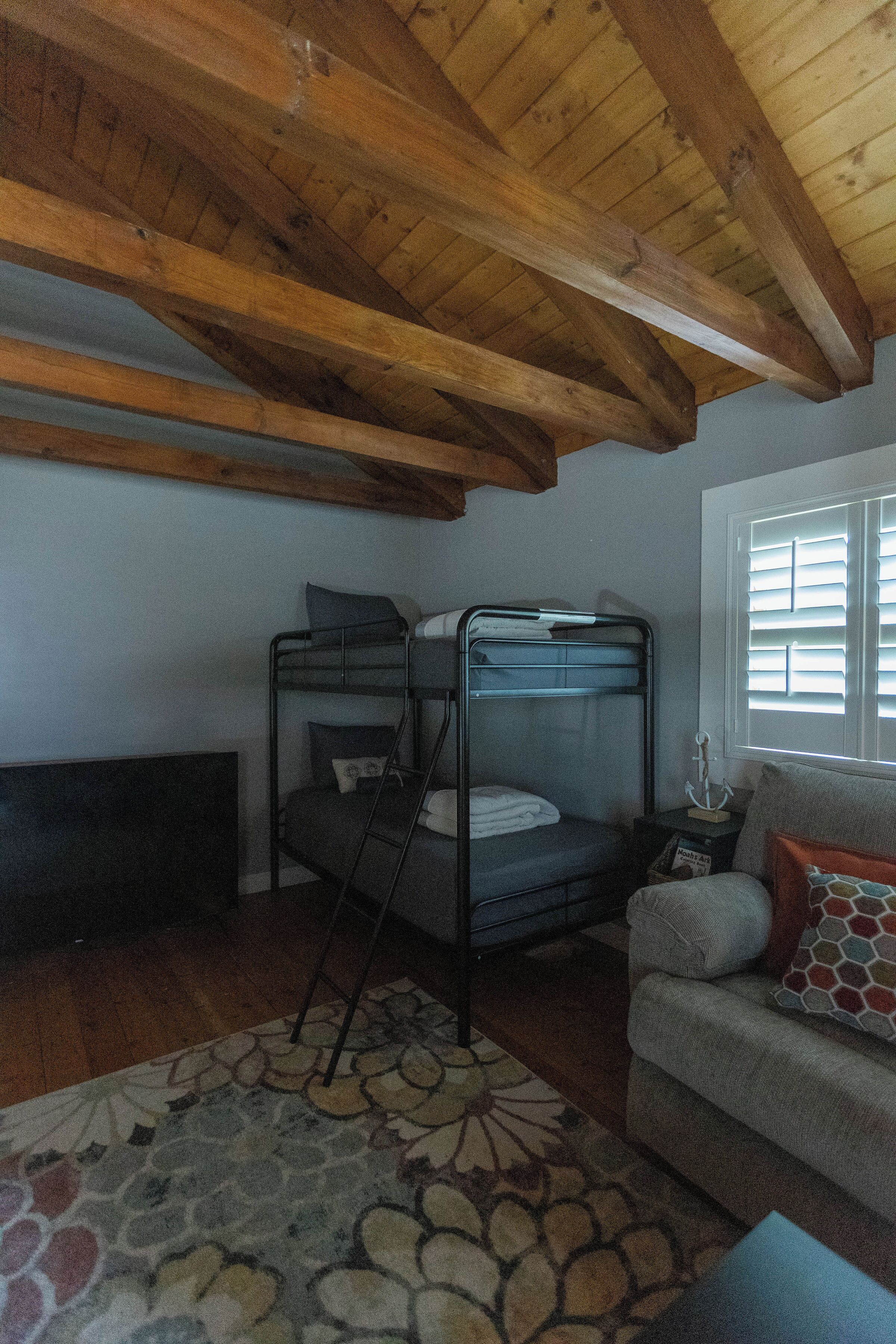 A room with a bunk bed, a sofa, a patterned rug, and a window with blinds.