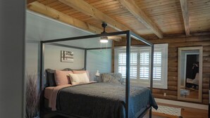 Un dormitorio con cama con dosel, vigas de madera, un ventanal y un espejo.