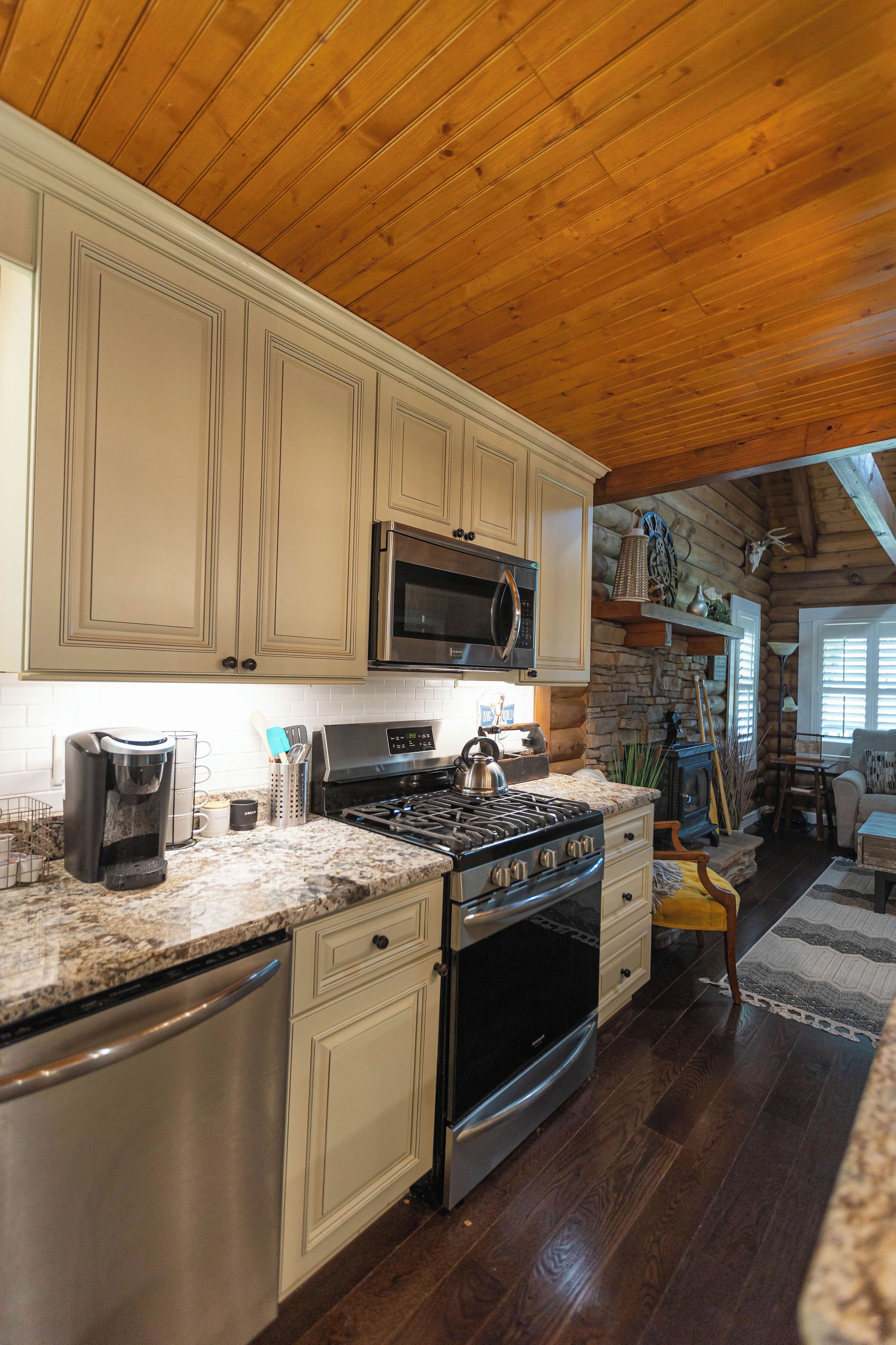 A kitchen with wooden ceiling, granite countertops, stainless steel appliances, and beige cabinetry.