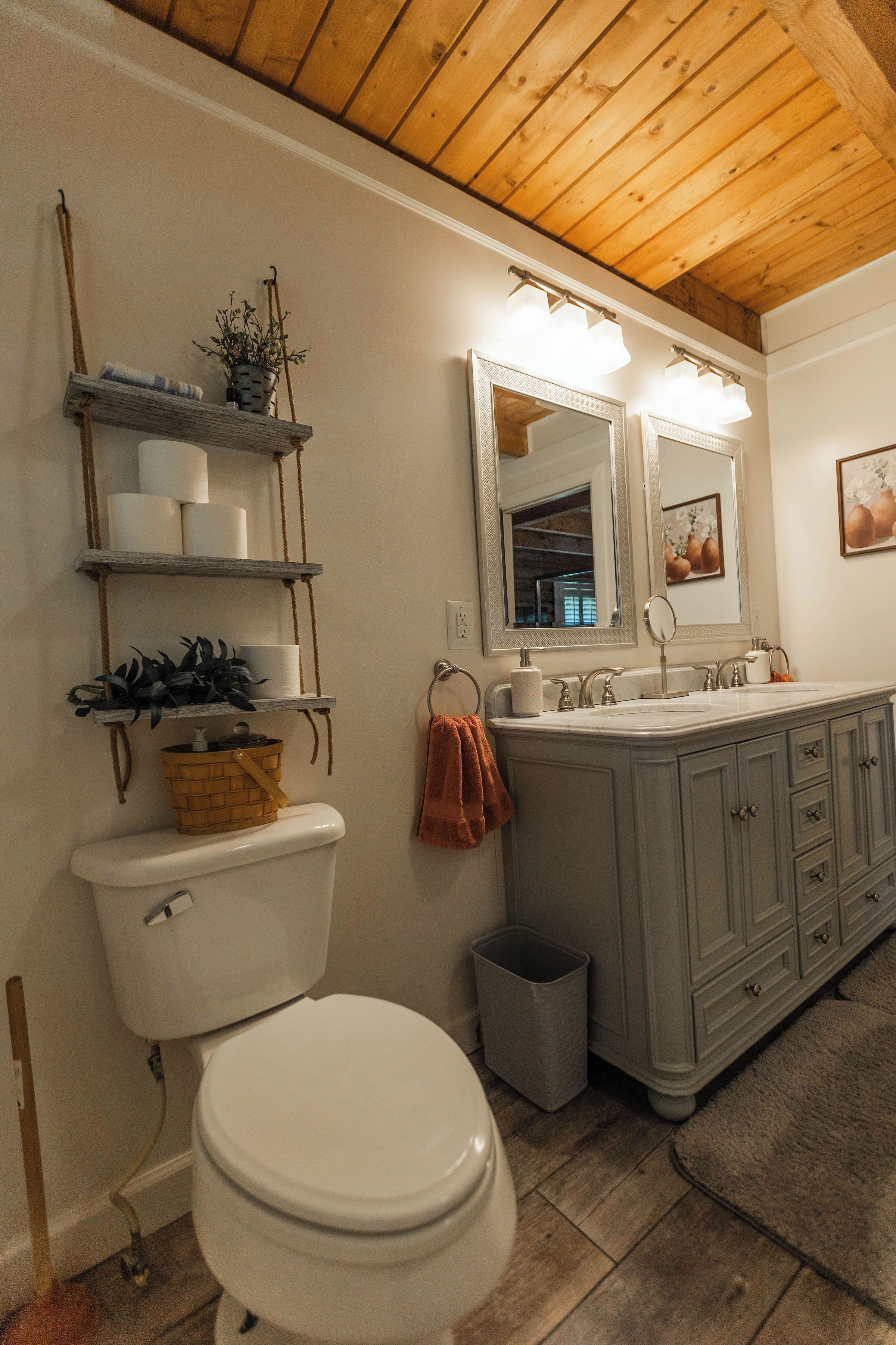 Ein Badezimmer mit Toilette, Waschbecken, Waschtisch, Regalen und einem Spiegel.