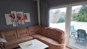 A modern living room with a brown sectional sofa, a white coffee table, and a large sliding glass door leading to an outdoor area with chairs. - Vacation apartment "Schöne Aussicht" with large balcony-terrace (Nordenham)