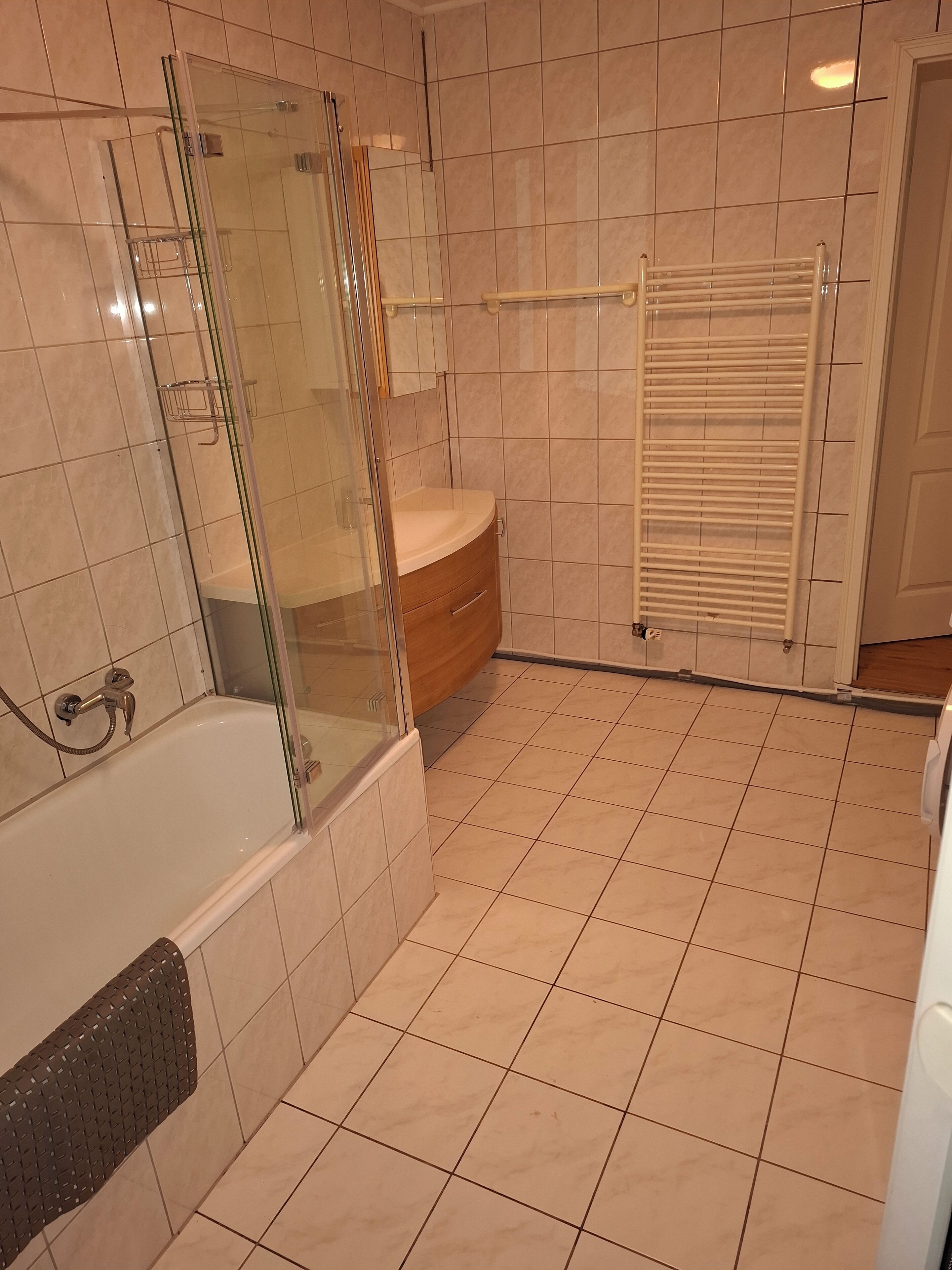 Ein modernes Badezimmer mit einer Glaskabine zur Dusche, einer weißen Badewanne und einem beige gefliesten Boden.