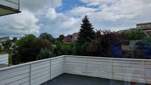 A rooftop terrace with a white railing, surrounded by greenery and buildings in the background. - Vacation apartment "Schöne Aussicht" with large balcony-terrace (Nordenham)