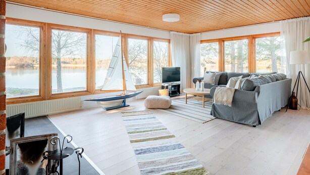 Un salón amplio con ventanas grandes, techo de madera, un sofá gris, un televisor y un modelo de velero.