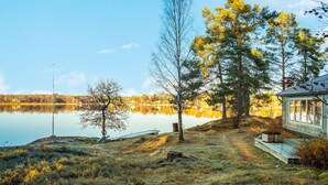 Una cabaña junto al lago con un muelle que se adentra en el agua, rodeada de árboles y un cielo despejado.