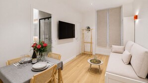 Una sala moderna con comedor, un televisor de pantalla plana en la pared, piso de madera y un ventanal grande.