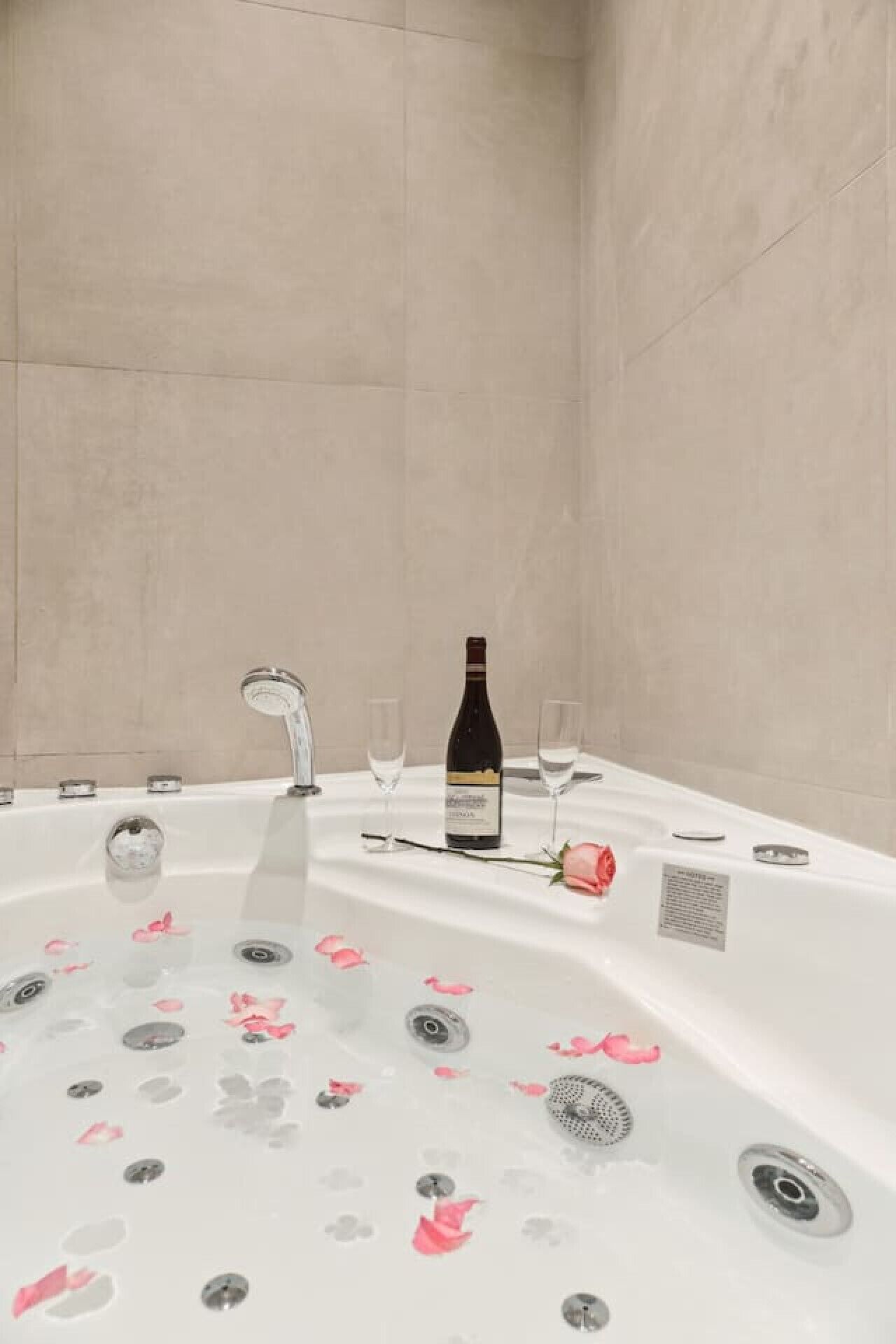 Eine Wellness-Badewanne mit Rosenblüten, einer Weinflasche und Gläsern auf einem weißen Tisch.