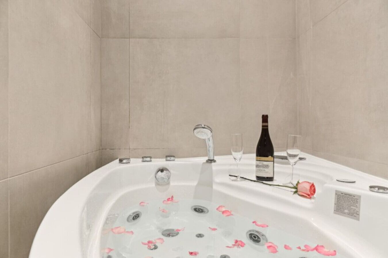 Une baignoire remplie de pétales de rose, une bouteille de vin et des verres.
