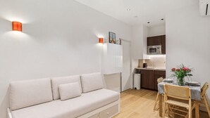 Una sala moderna con sofá, una mesa de comedor con sillas, una zona de cocina con microondas y un pequeño cubo de basura.