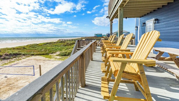 Een houten terras met strandstoelen en een volleybalnet met uitzicht op het strand.