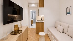 A modern, compact living space with a flat-screen TV, kitchenette, and a sofa.