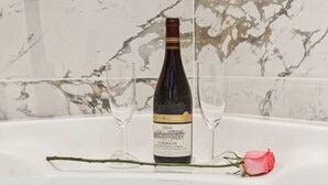 A bottle of wine on a table with two glasses and a rose.