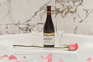A bottle of wine on a table with two glasses and a rose.