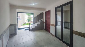 Un couloir avec un sol carrelé, un escalier, une porte rouge et un grand miroir sur le côté droit.