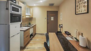 Une cuisine compacte équipée d’un réfrigérateur, d’un four à micro-ondes, d’une cuisinière et d’un évier. On y trouve une table à manger avec des chaises, et un tableau représentant des motifs botaniques est accroché au mur.