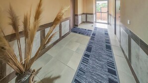 Un couloir avec un tapis à motifs, un vase contenant des plumes d’herbe des pampas et une vue sur l’extérieur.