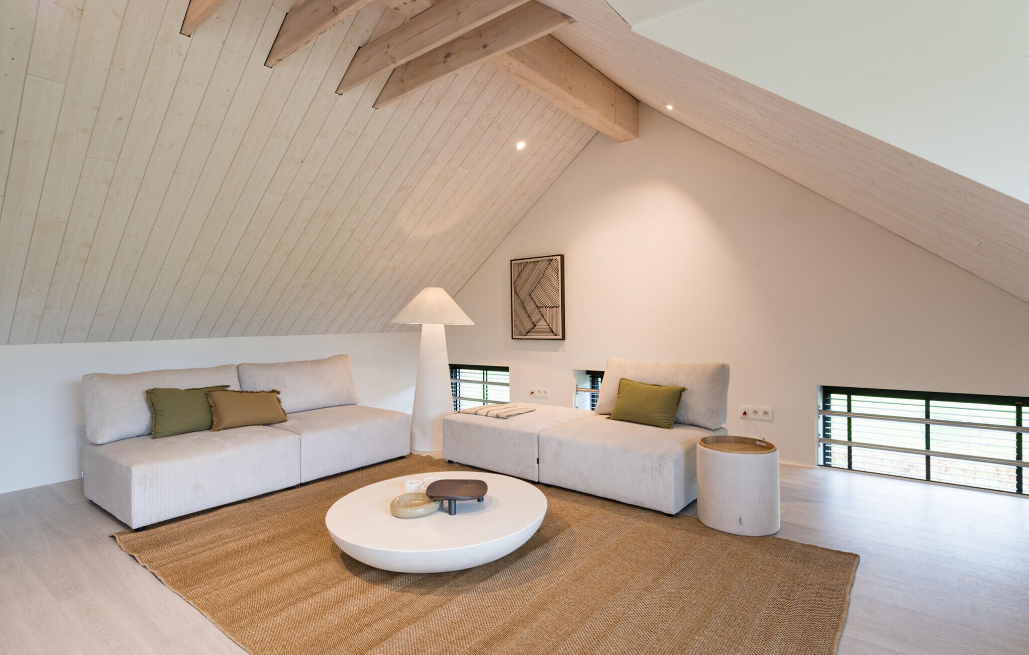 Une chambre de style loft moderne, avec un plafond en pente, une grande fenêtre, une table basse ronde et un design minimaliste.