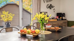 Ein Esstisch mit einer Obstschale, einer Vase mit gelben Blumen und einer Kaffeebar im Hintergrund.