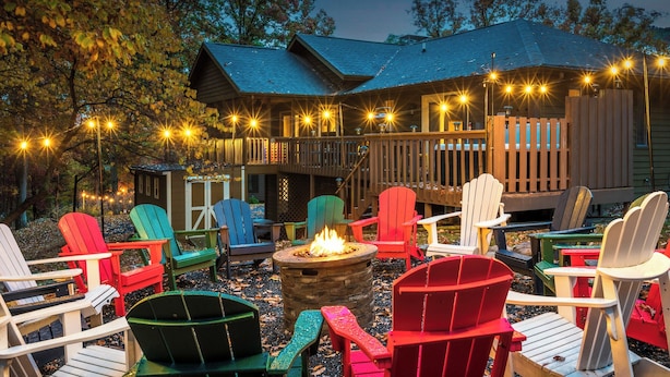 Ein gemütlicher Außenbereich mit Adirondack-Stühlen und einem Feuerkorb, umgeben von einer Holzterrasse und Lichterketten.