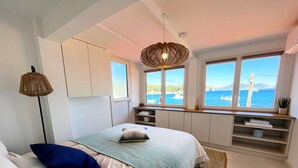 A bedroom with a bed, bedside lamps, a view of the sea, and built-in storage. - A little corner of paradise (Toulon)