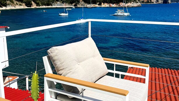 A boat deck with a white cushioned chair, a red railing, and a view of the sea with boats and a rocky coastline. - A little corner of paradise (Toulon)
