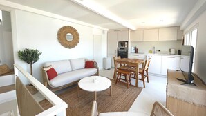 A modern kitchen with white cabinets, a dining area with a round table, and a living room with a sofa and a decorative wall hanging. - A little corner of paradise (Toulon)