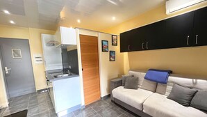 Un espace de vie compact comprenant un coin cuisine, un canapé et une porte donnant sur une autre pièce.