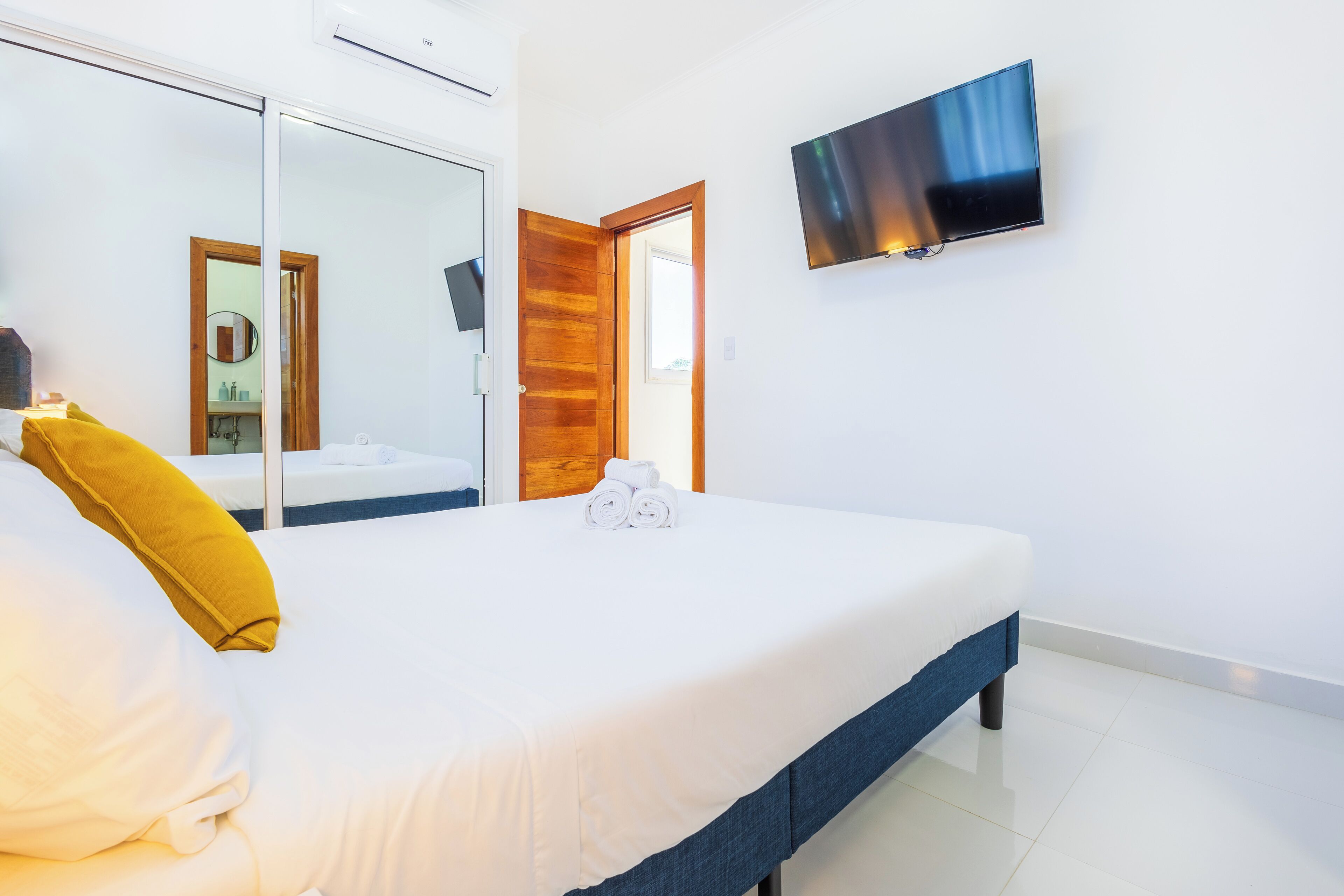 A hotel room with a bed, a TV mounted on the wall, and a mirror reflecting the room.