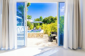 Une chambre moderne dotée d’une porte-fenêtre coulissante qui donne sur un espace extérieur aménagé avec une piscine, des chaises longues et des plantes en pot.
