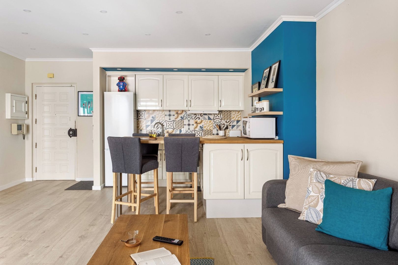 Un espacio habitable compacto con kitchenette, una zona de comedor con dos sillas, un sofá con cojines y una mesa de centro de madera.