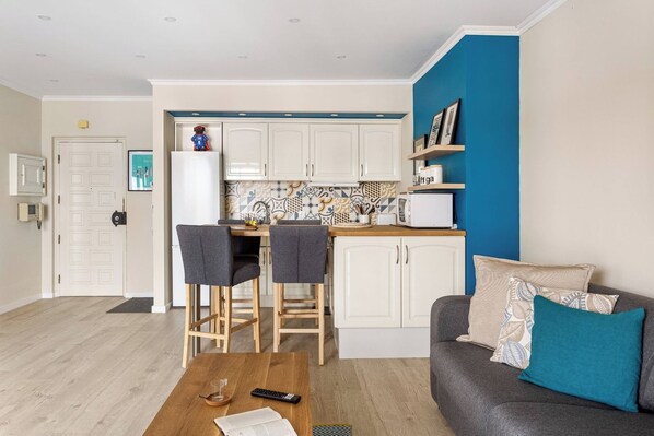 A compact living space with a kitchenette, a dining area with two chairs, a sofa with cushions, and a wooden coffee table.