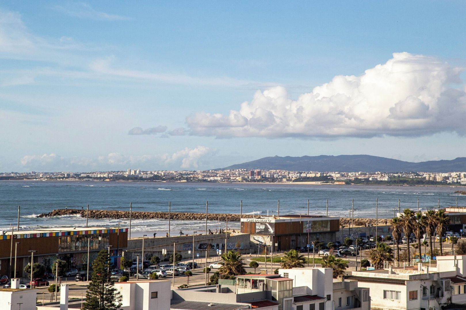 Un paisaje costero con playa, un café y vistas a montañas distantes.