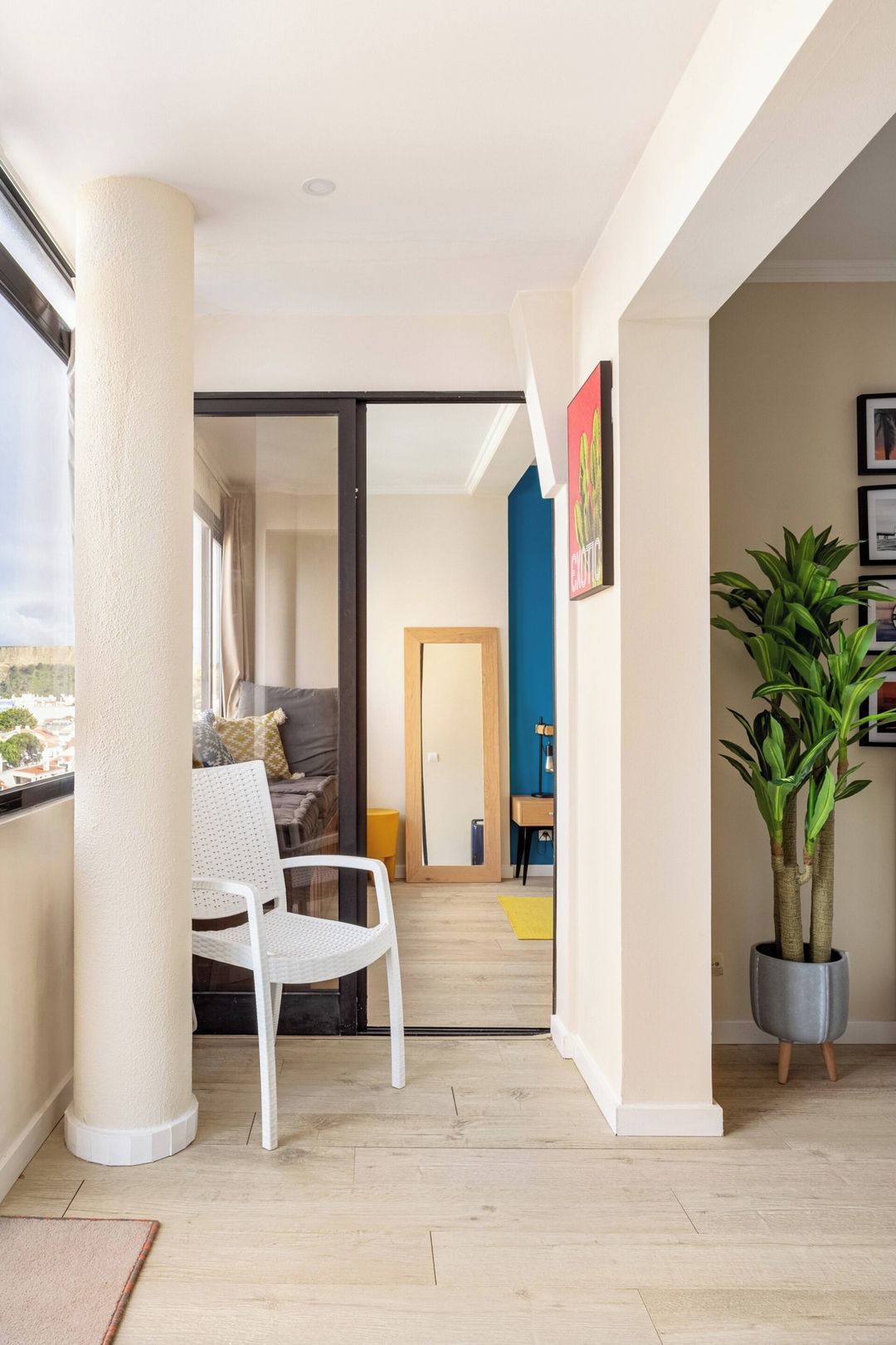 A modern interior with a white chair, a potted plant, and a view through a glass door.