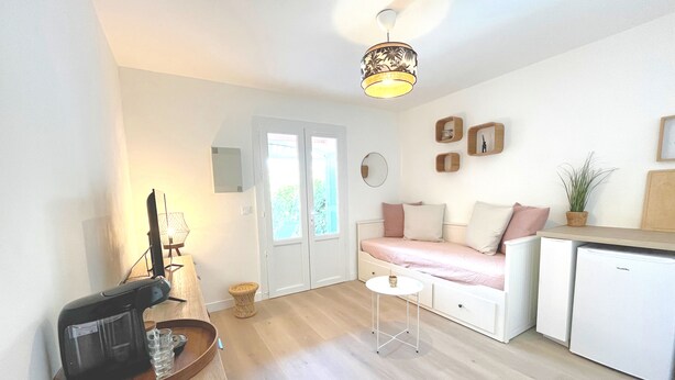 Een knus woongedeelte met kitchenette, een bank, een klein tafeltje en een plafondlamp.