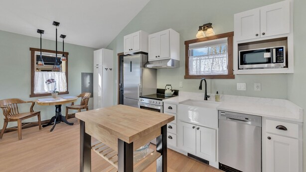 A modern kitchen with white cabinets, stainless steel appliances, a wooden dining table, and pendant lights. - New! Charming private home in historic district. Short walk to downtown Rapid City. Well-appointed and newly renovated. King bed, fireplace, dishwasher, washer/dryer, Wi-Fi, EV charger, tiled shower. Off-street parking. Easy access to I-90. (Rapid City)
