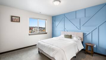 Une chambre avec une grande fenêtre, un lit recouvert de draps blancs, un mur d’accent bleu et un petit tabouret en bois.