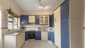 A kitchen with blue and cream cabinets, a stove, microwave, and a hanging plant.