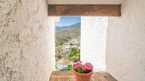 A balcony with a potted plant, a thatched umbrella, and a view of a hillside town. - Juan Manuel - Los Mangos El Borge by Ruralidays (Málaga)
