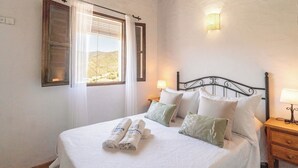 A neatly made bed with pillows and towels, a window with curtains, a wall-mounted lamp, and a bedside table with a lamp. - Juan Manuel - Los Mangos El Borge by Ruralidays (Málaga)