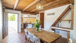 Een eetruimte met een houten tafel en stoelen, een hanglamp en een haard van baksteen.