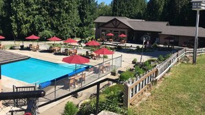 A pool area with red umbrellas, lounge chairs, and a building with a sloped roof. - Mara Spring Lodges - Lodge 1 (Mara)