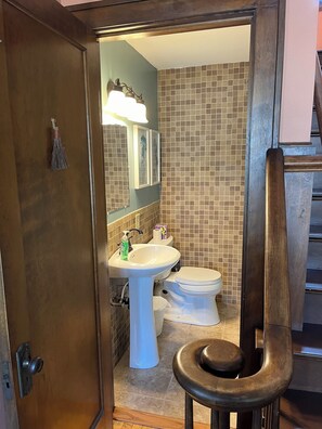 A bathroom with a wooden door, a white sink, a toilet, and a mirror with framed artwork.