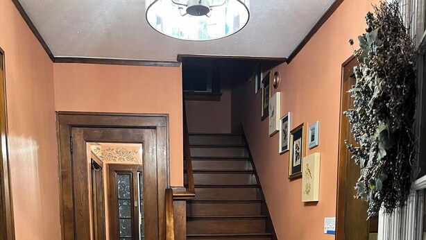 A wooden staircase leading to a second floor, with a patterned rug at the bottom and a door with a decorative mirror on the left. - Cheerful home away from home in welcoming Wausau!  (Wausau)