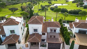 A residential area with houses featuring terracotta roofs and white walls, overlooking a golf course with well-maintained lawns and trees.