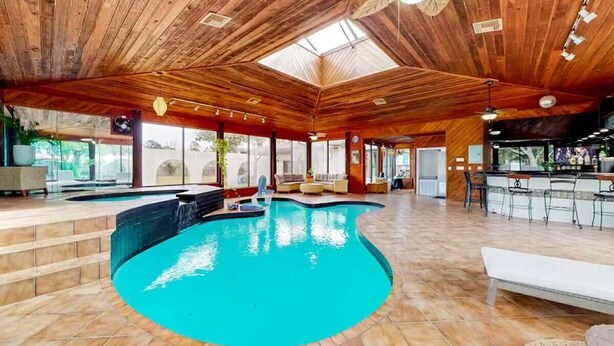 An indoor swimming pool with wooden ceiling and tiled floor, surrounded by seating areas and a bar. - Pool, Beaches, OWA, Dining, and More | Palmaway (Foley)